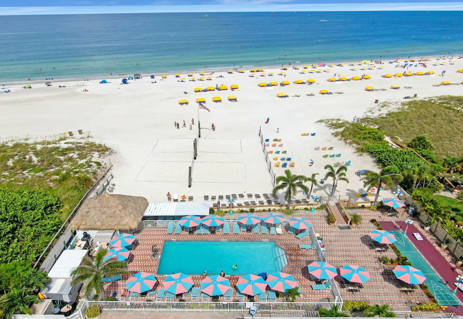 A balcony view showcasing a beach and pool at Plaza Beach Resorts, St. Pete Beach, Florida, under a clear blue sky.